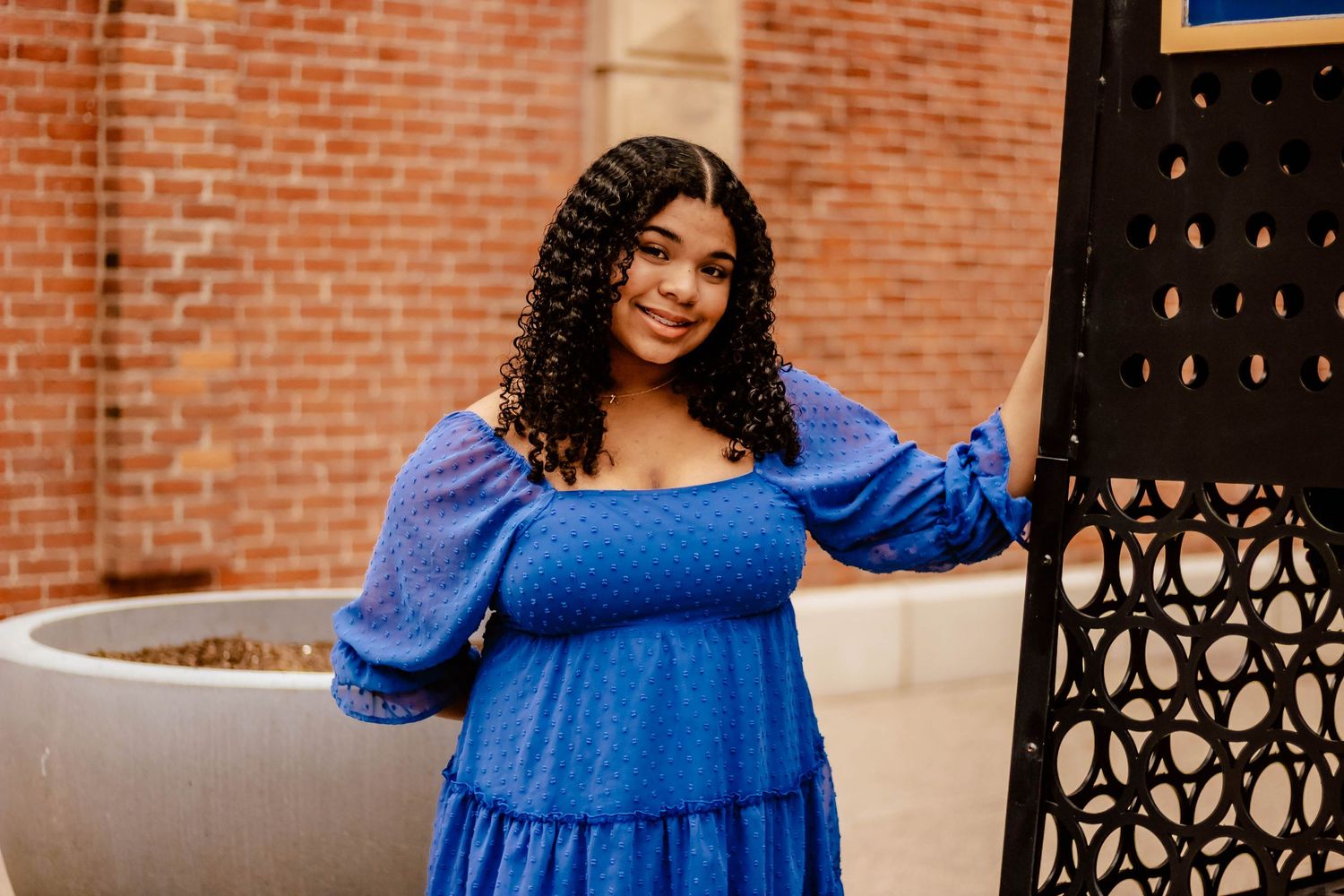 Portrait featuring a blue puff sleeve dress against a brick building backdrop.