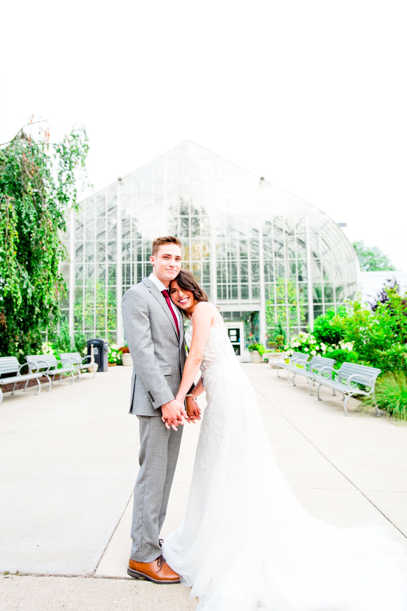bride lays on groom's chest and they smile in front of Krohn Conservatory for summer wedding in Cincinnati