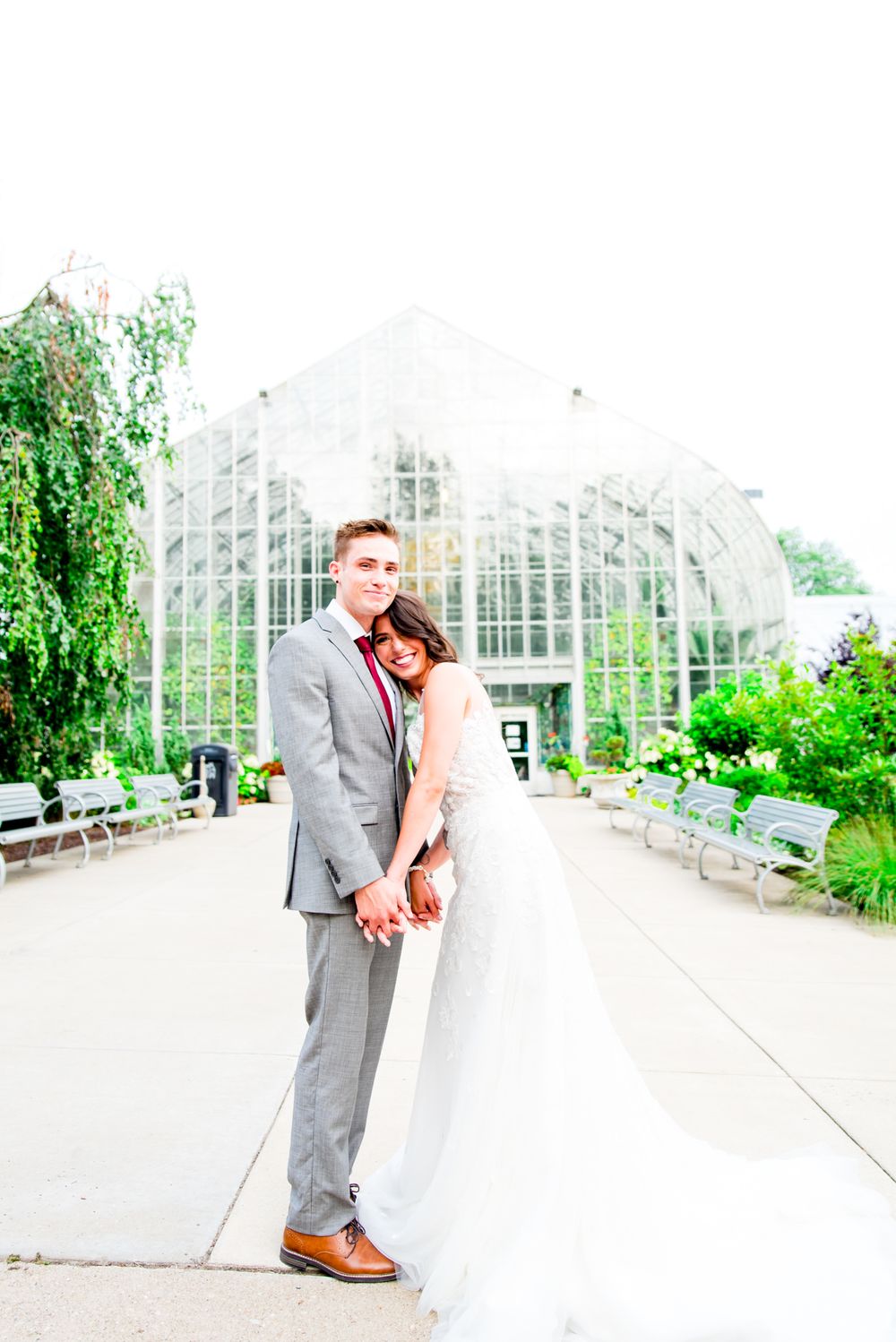 bride lays on groom's chest and they smile in front of Krohn Conservatory for summer wedding in Cincinnati