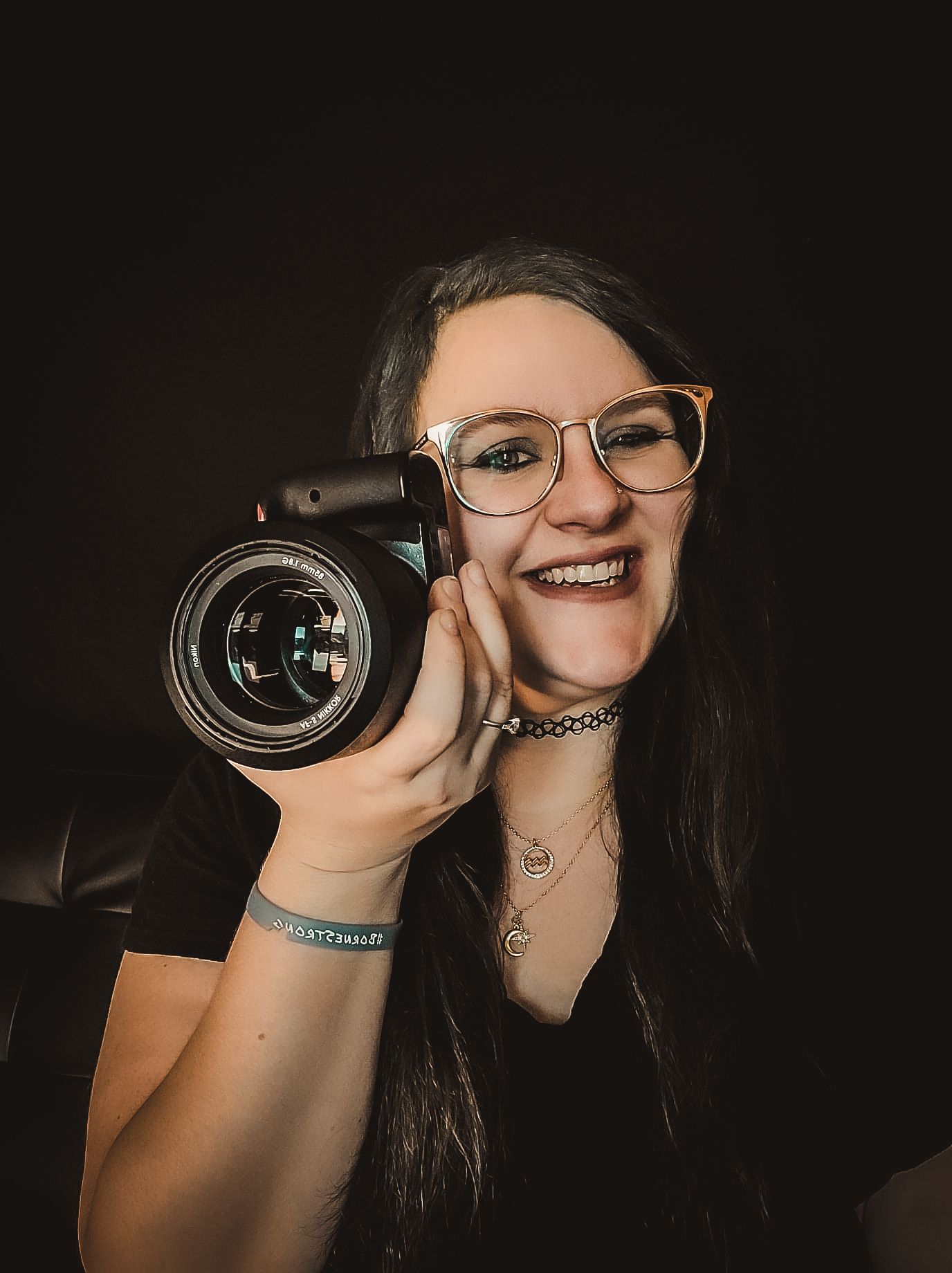 Portrait of smiling photographer with glasses holding professional camera against dark background.