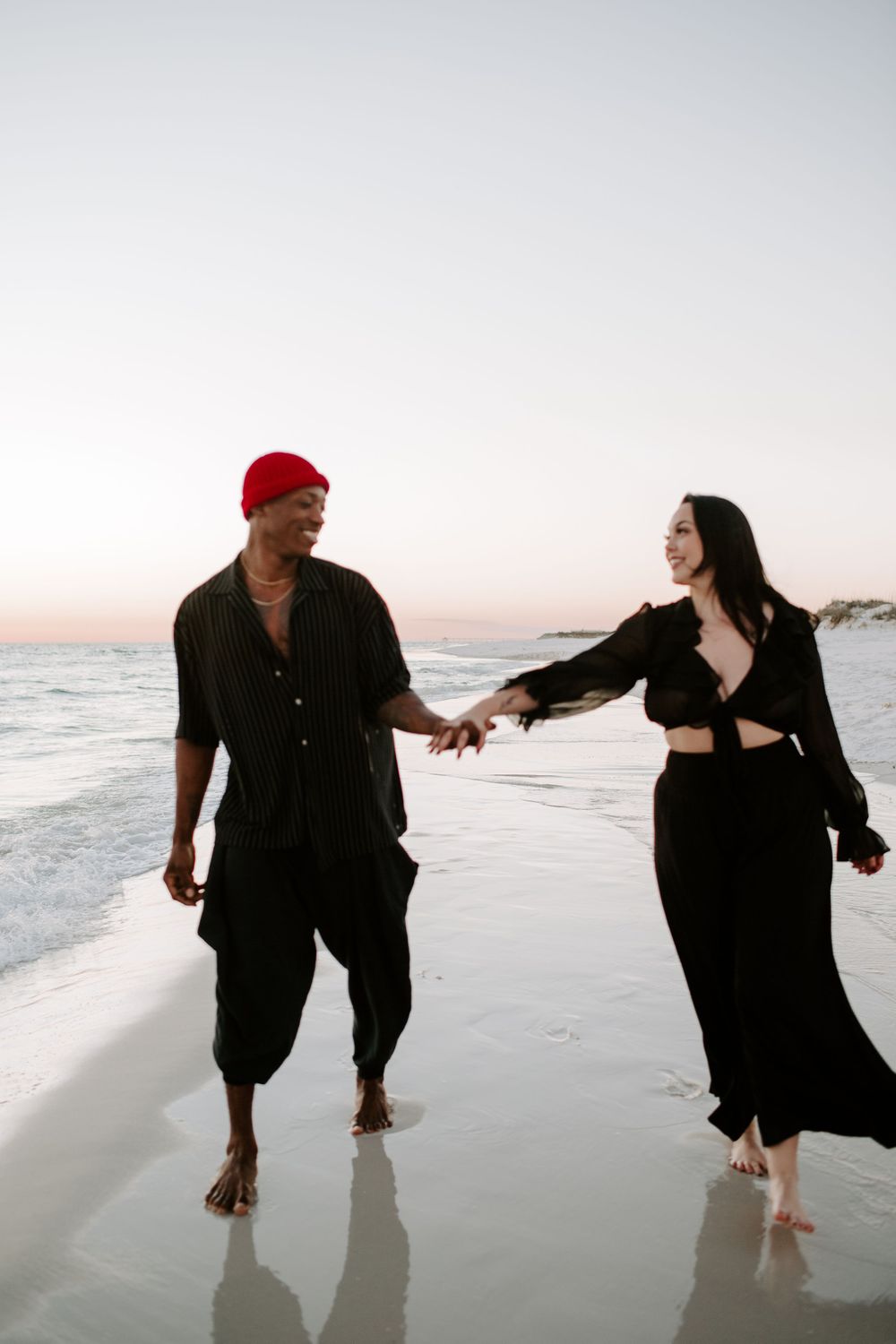 couple holding hands and walking on the beach laughing during their Fort Walton Beach photoshoot