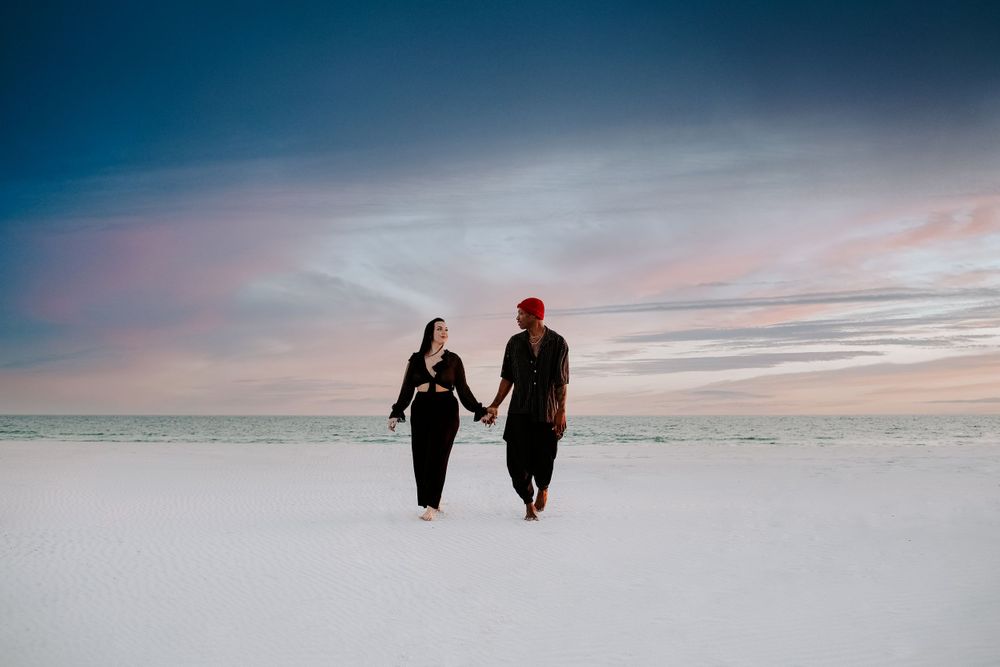couple holding hands walking away from the ocean during their beach photoshoot