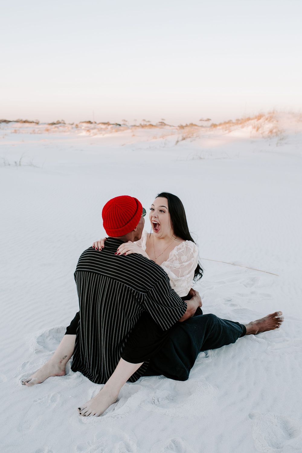 woman making a face as she and her boyfriend are sitting in the sand