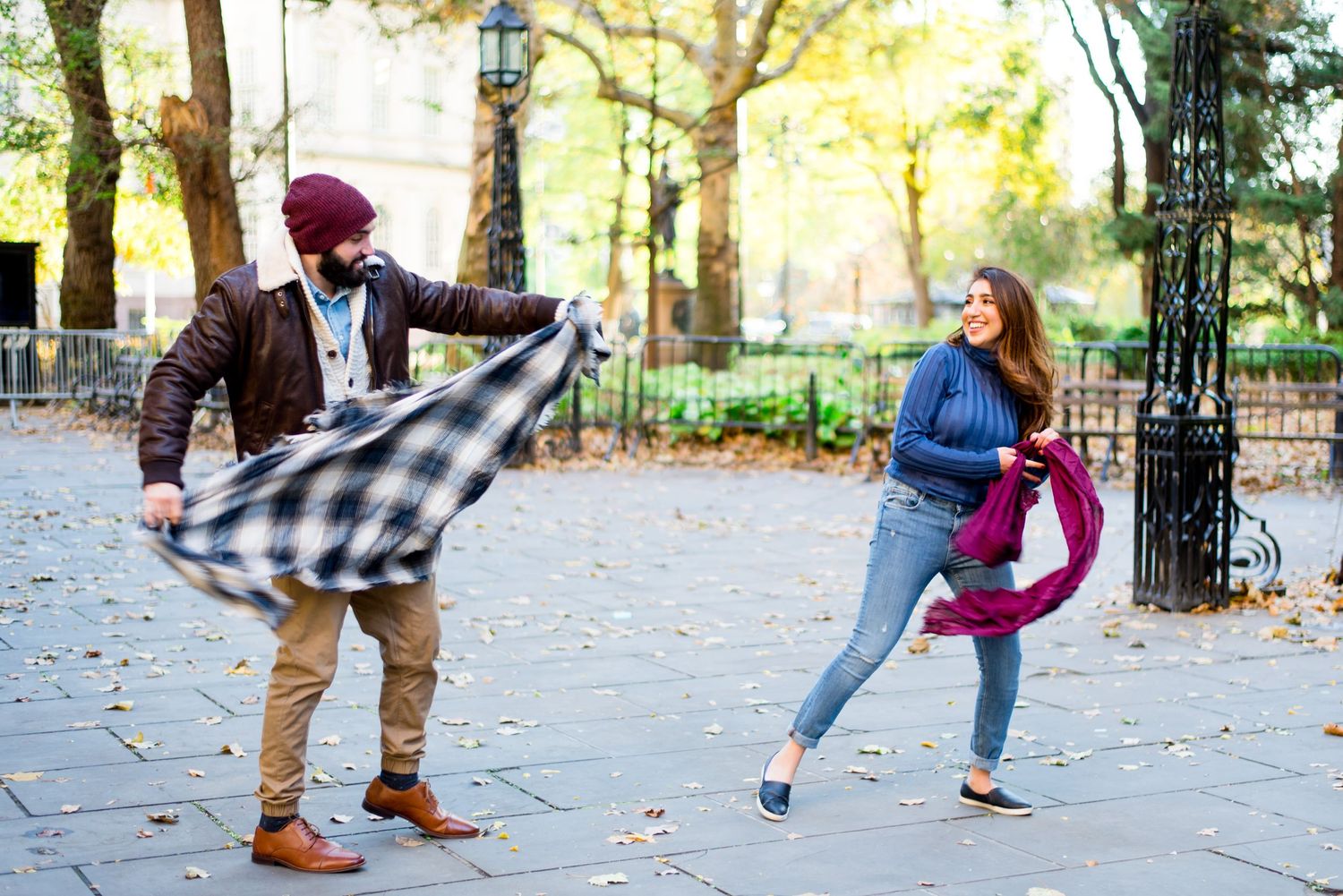 young engaged couple smiles and throws their scarves at each other for engagement pictures in NYC Manhattan