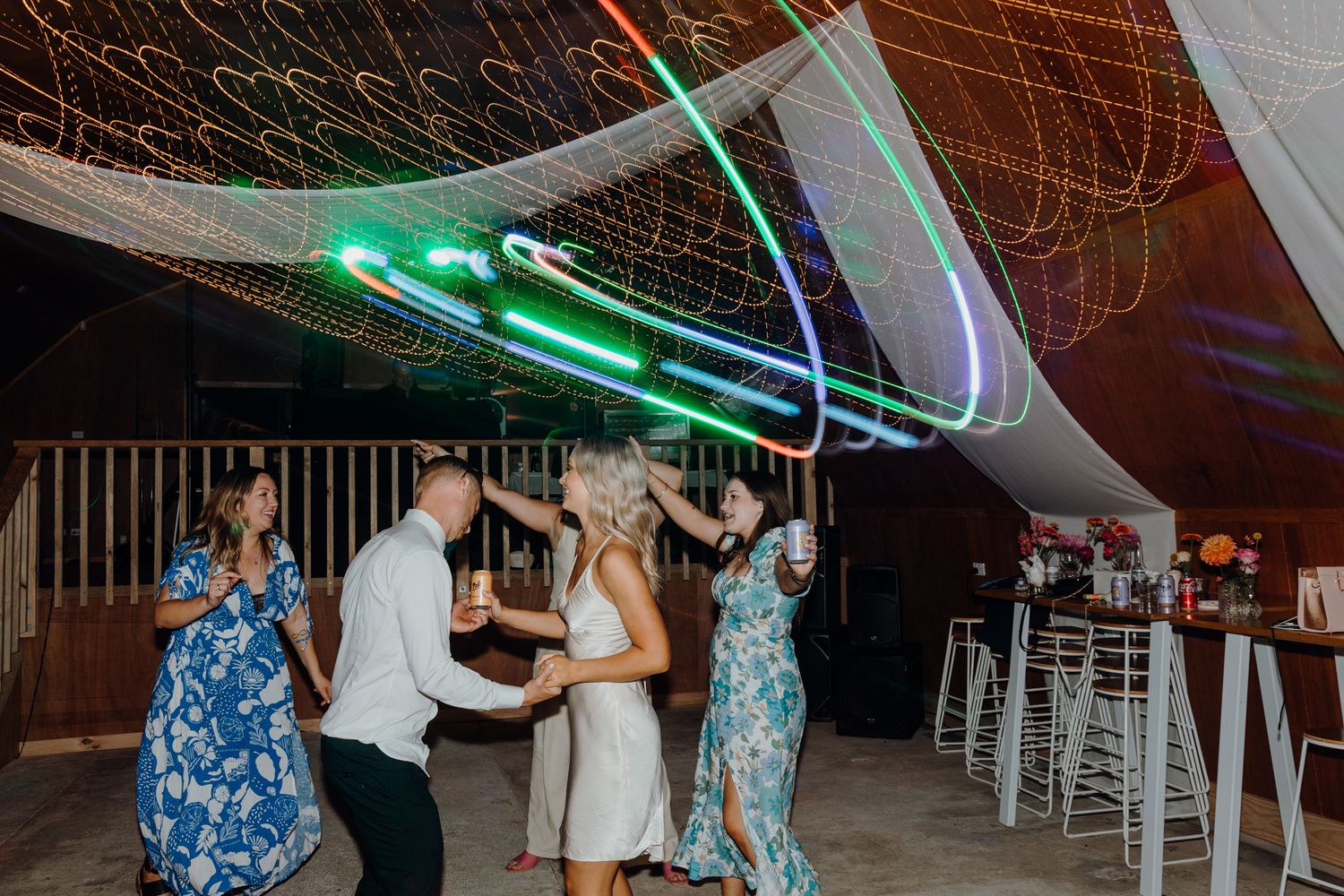 Wedding celebration with guests dancing under modern LED lighting and white ceiling drapes.