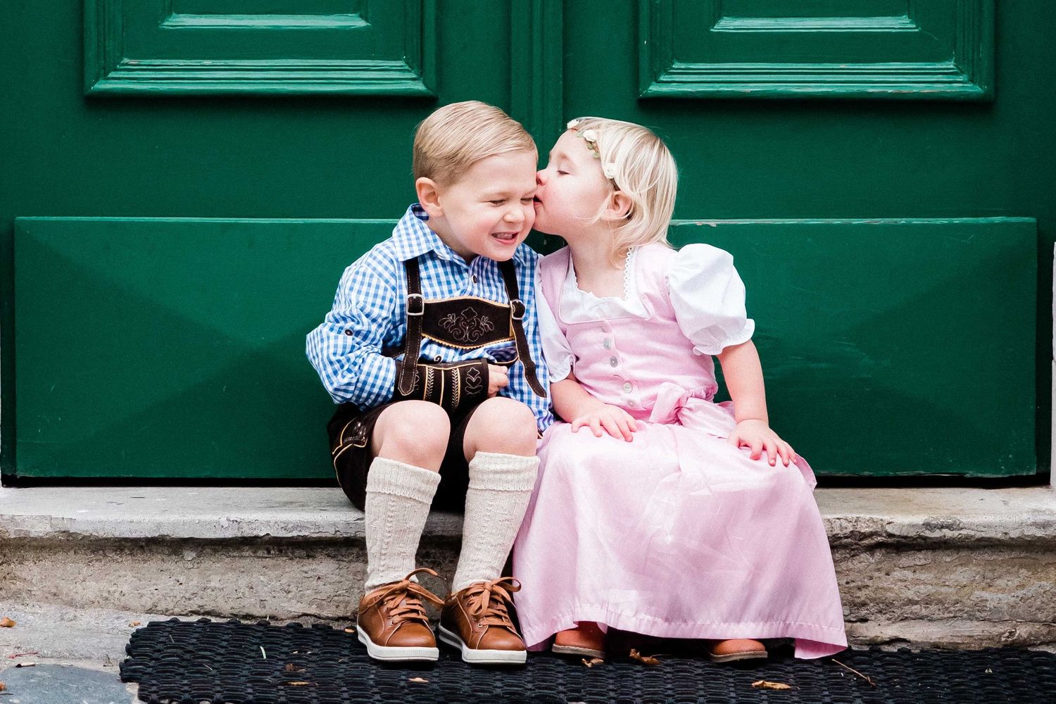 Children sitting in Vienna in front of a green door wearing traditional outfit Lederhosen and Dirndl
