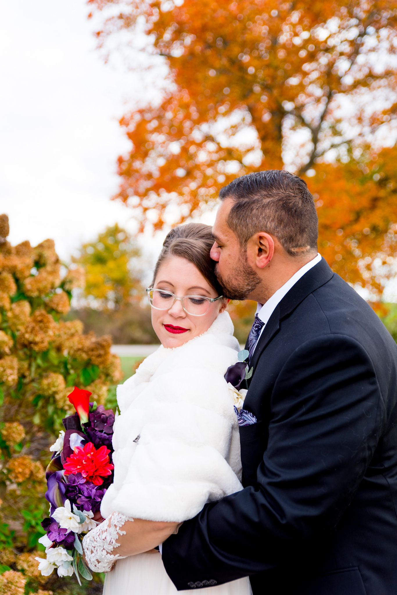groom kissing brides forehead and bride in red lipstick closes her eyes in front of orange tree at November wedding