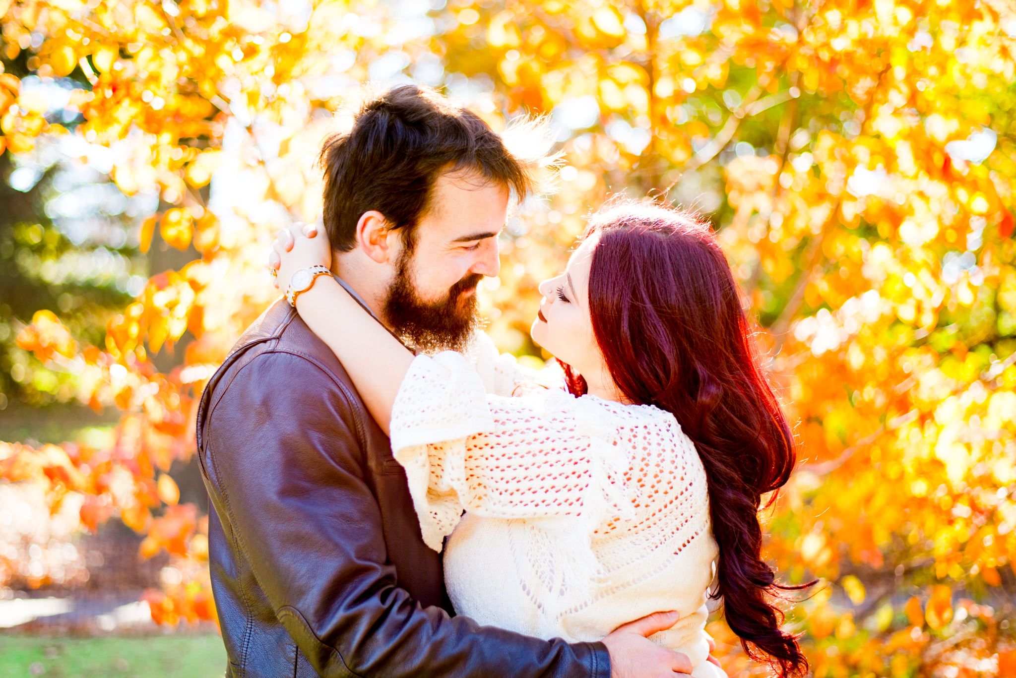 woman with red hair in white sweater looks at man in brown leather jacket with brown hair in Central Park at sunrise