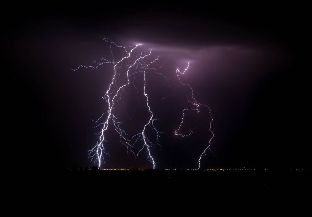 Multiple purple lightning bolts illuminate the dark night sky.