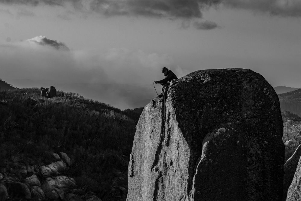 Silhouette of a rock climber perched atop a steep cliff face against a moody sky.
