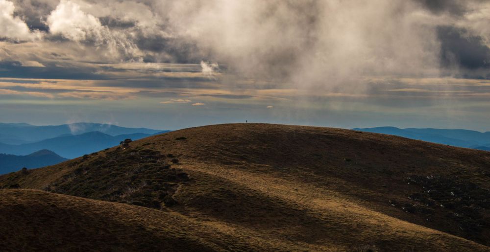 Rolling hills under dramatic cloudy skies with mountains in the distance.