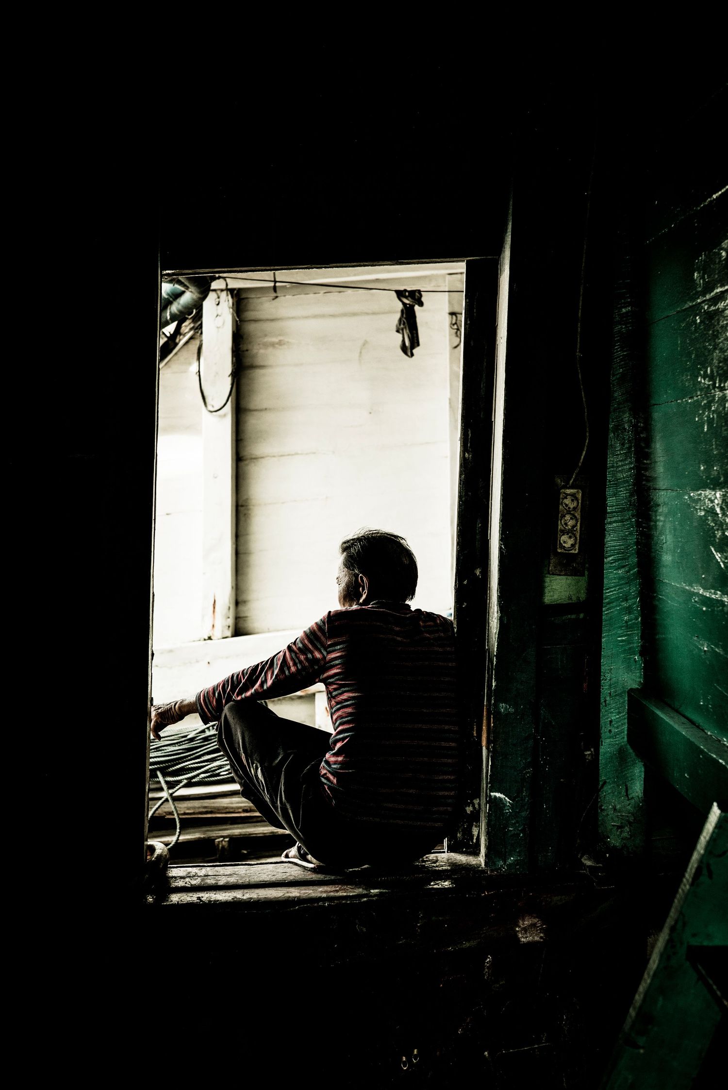 Man sitting in doorway on board traditional Pinisi, or Junk in Pelabuhan Sunda Kelapa Indonesia