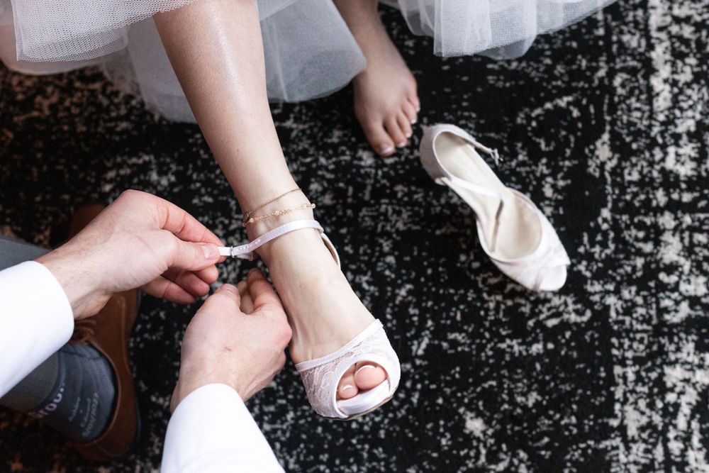 A close up of a groom's hands slipping a shoe on his bride's foot.