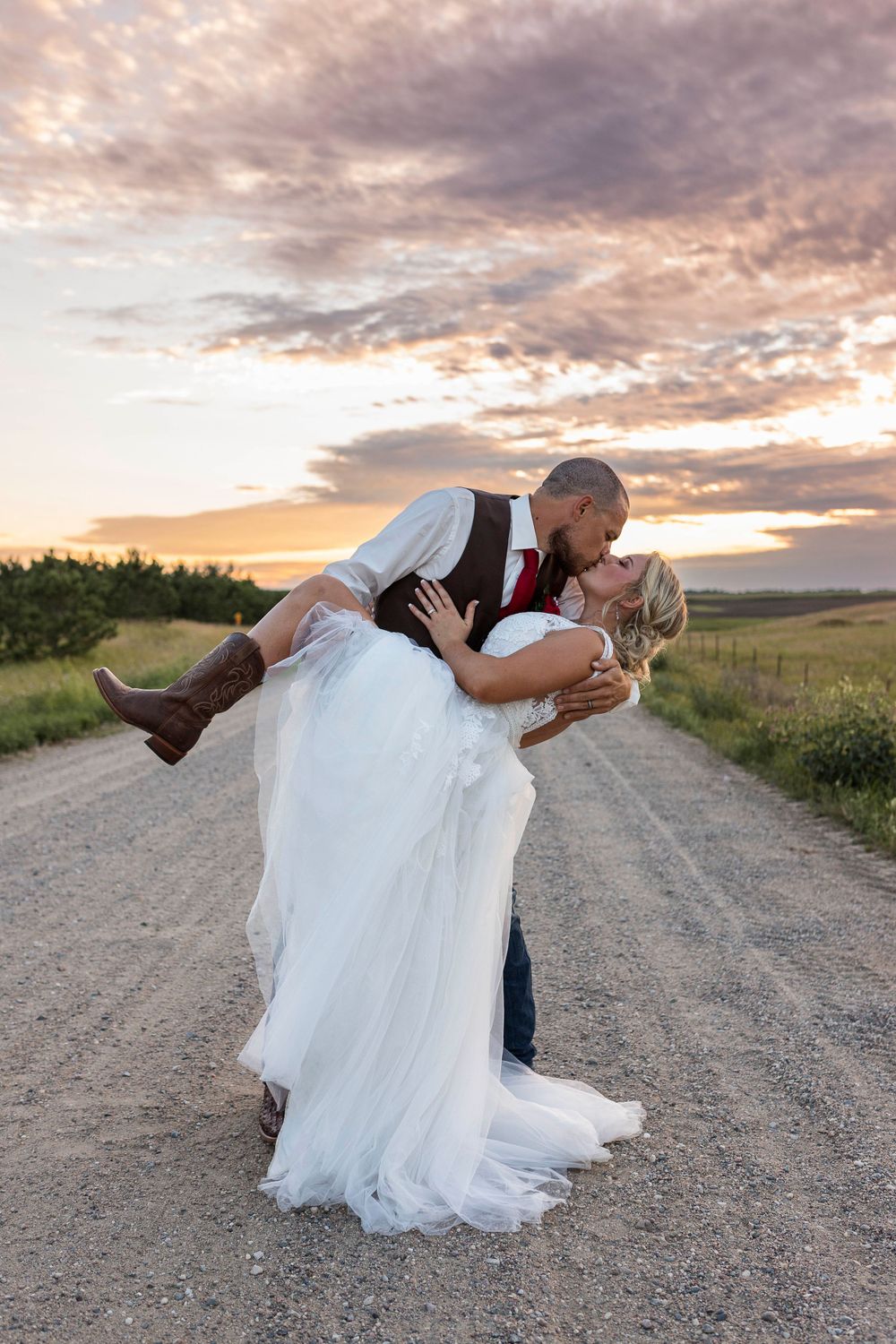 A bride with cowboy boots being dipped and kissed by her groom during a golden hour on a gravel road in Central, MN