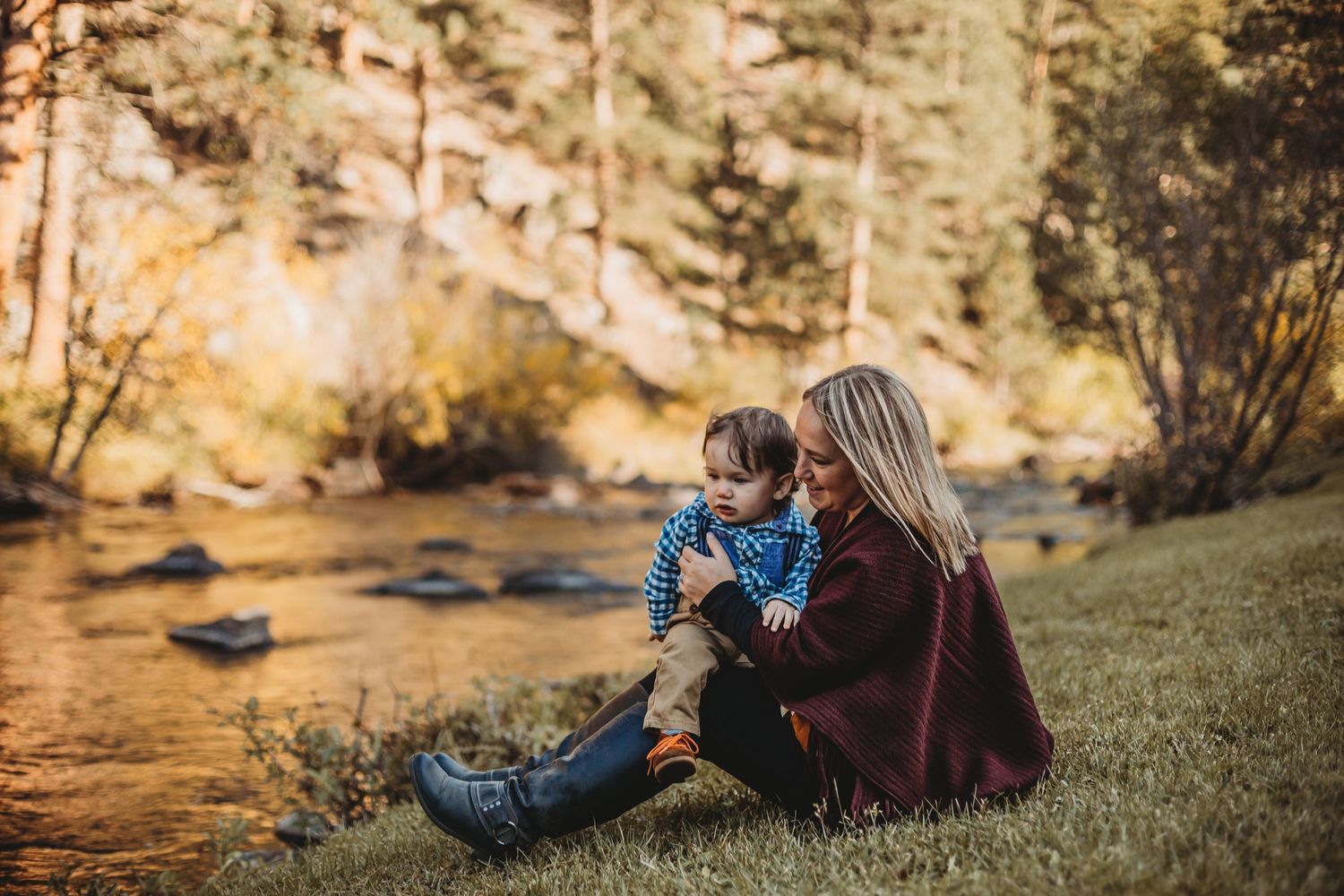 Mom and son sit by a river in the Rocky Mountains