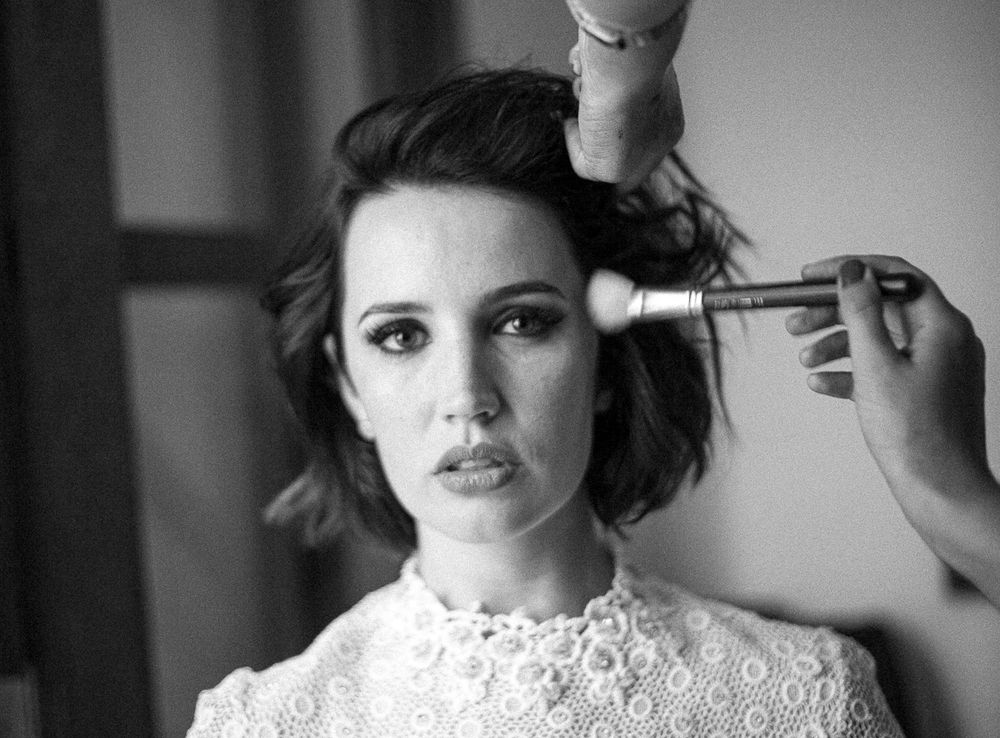 Black and white image of someone getting their hair styled while wearing a lace dress.