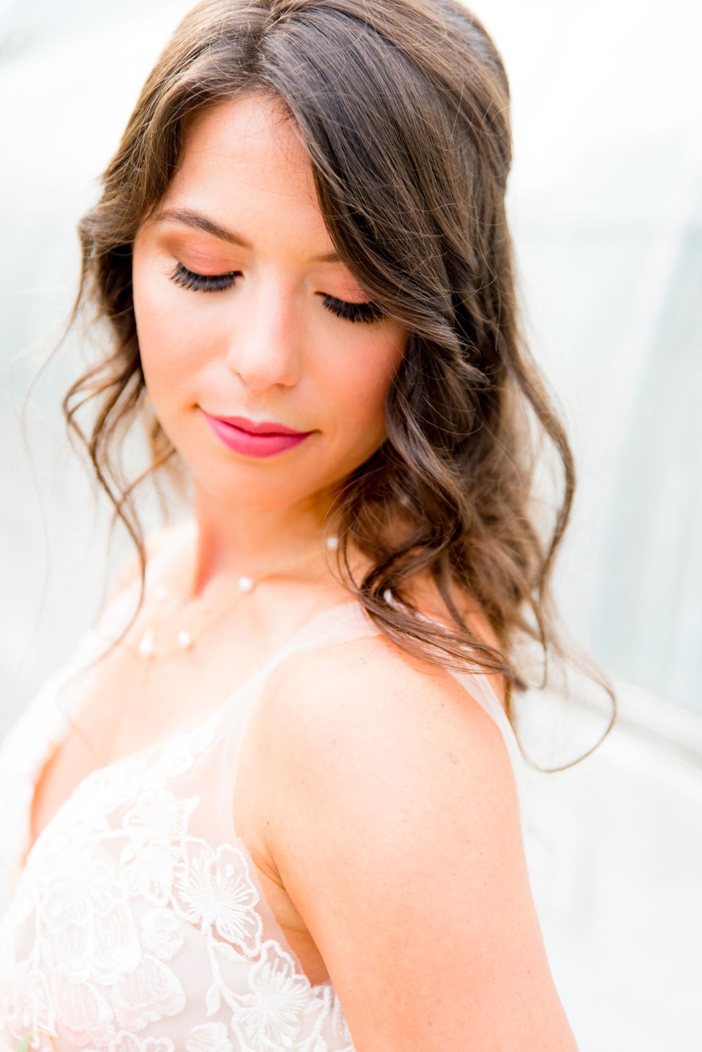 bride in pink lipstick, lace wedding gown, and pearl necklace in front of all white Krohn Conservatory wedding