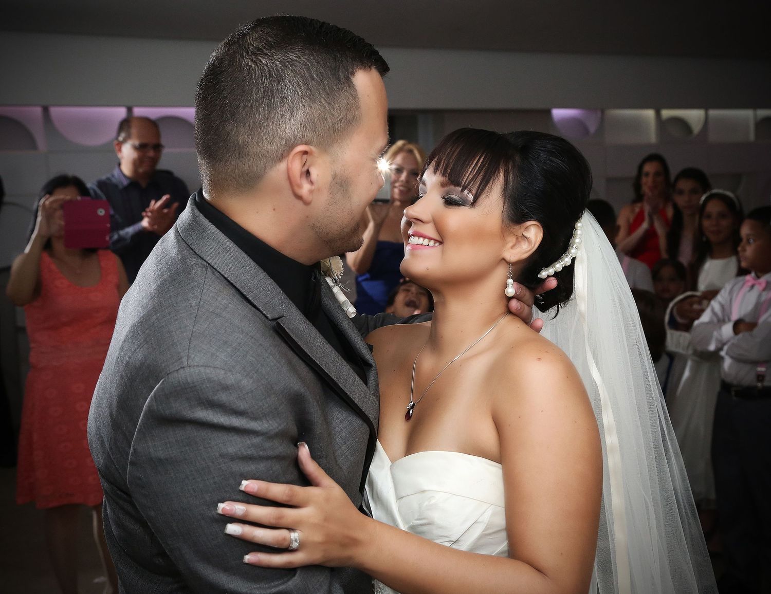 A couple shares an intimate dance moment at their wedding reception with onlookers in the background.