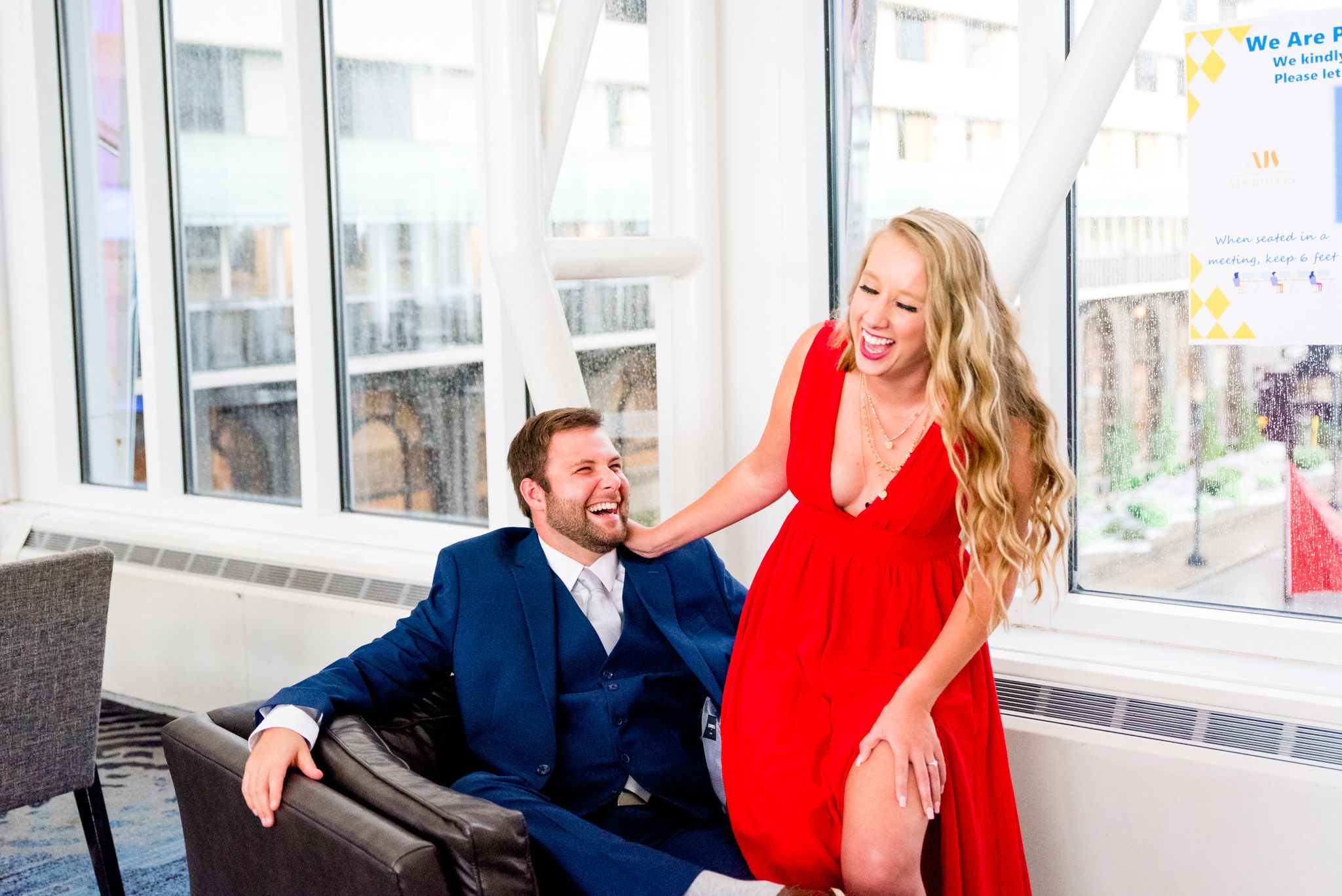 blonde woman in red dress laughing with fiance in navy suit at Galt House Hotel engagement pictures