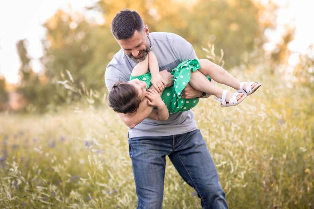 dad holding daughter in field tickling, laughing