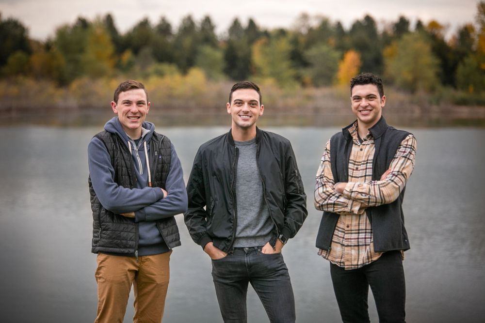 three brothers with fall layers posing near water