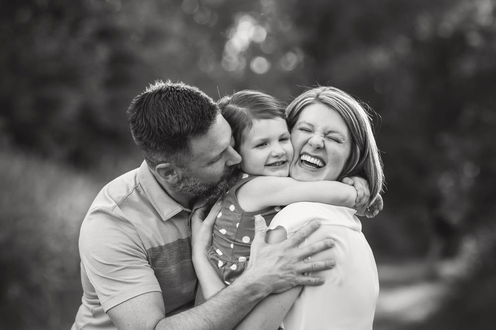 black and white image of mom, dad, and daughter laughing and hugging