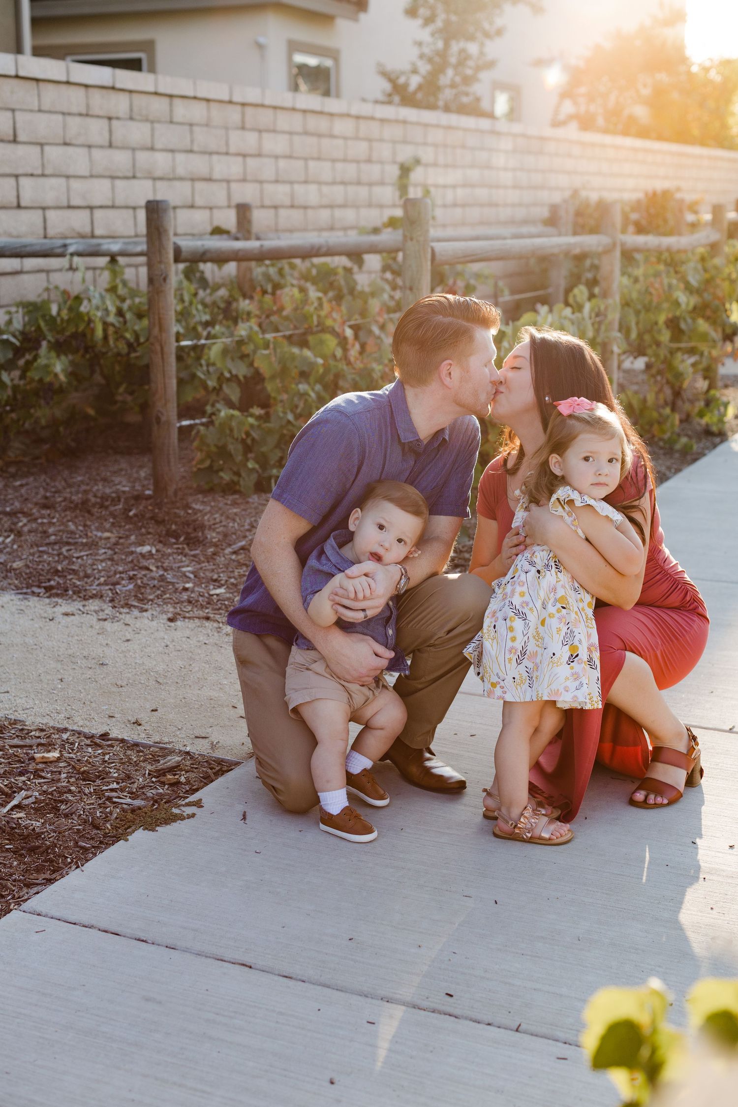 Young family at sunset mom dad kissing 2 kids