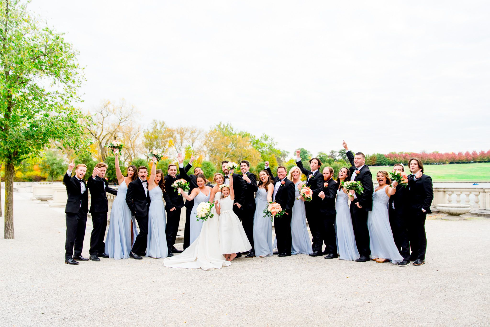 large wedding party in black suits and light blue dresses cheer on bride and groom at Forest Park in St. Louis