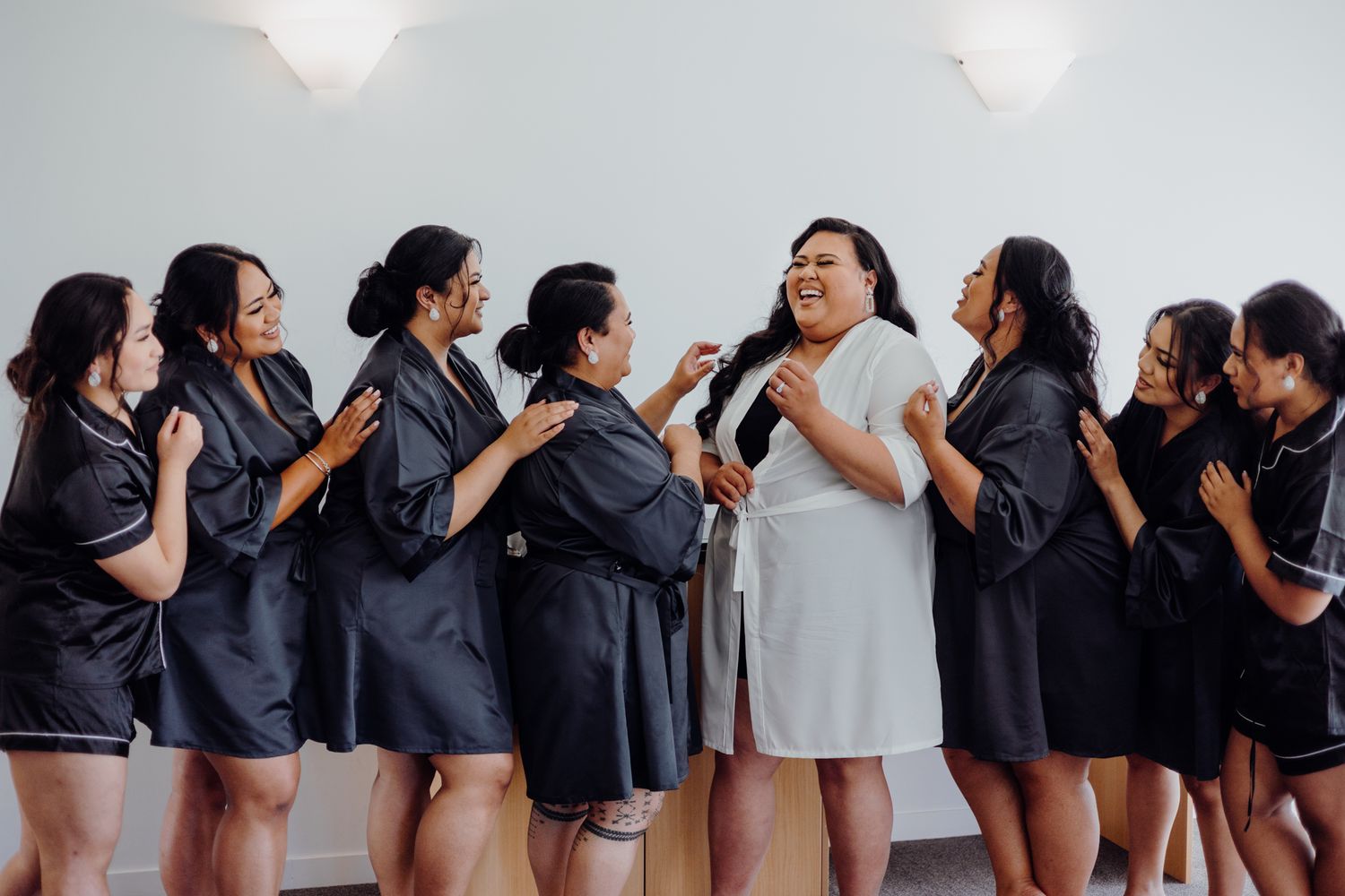 Wedding party in black dresses sharing excited moment with person in white.