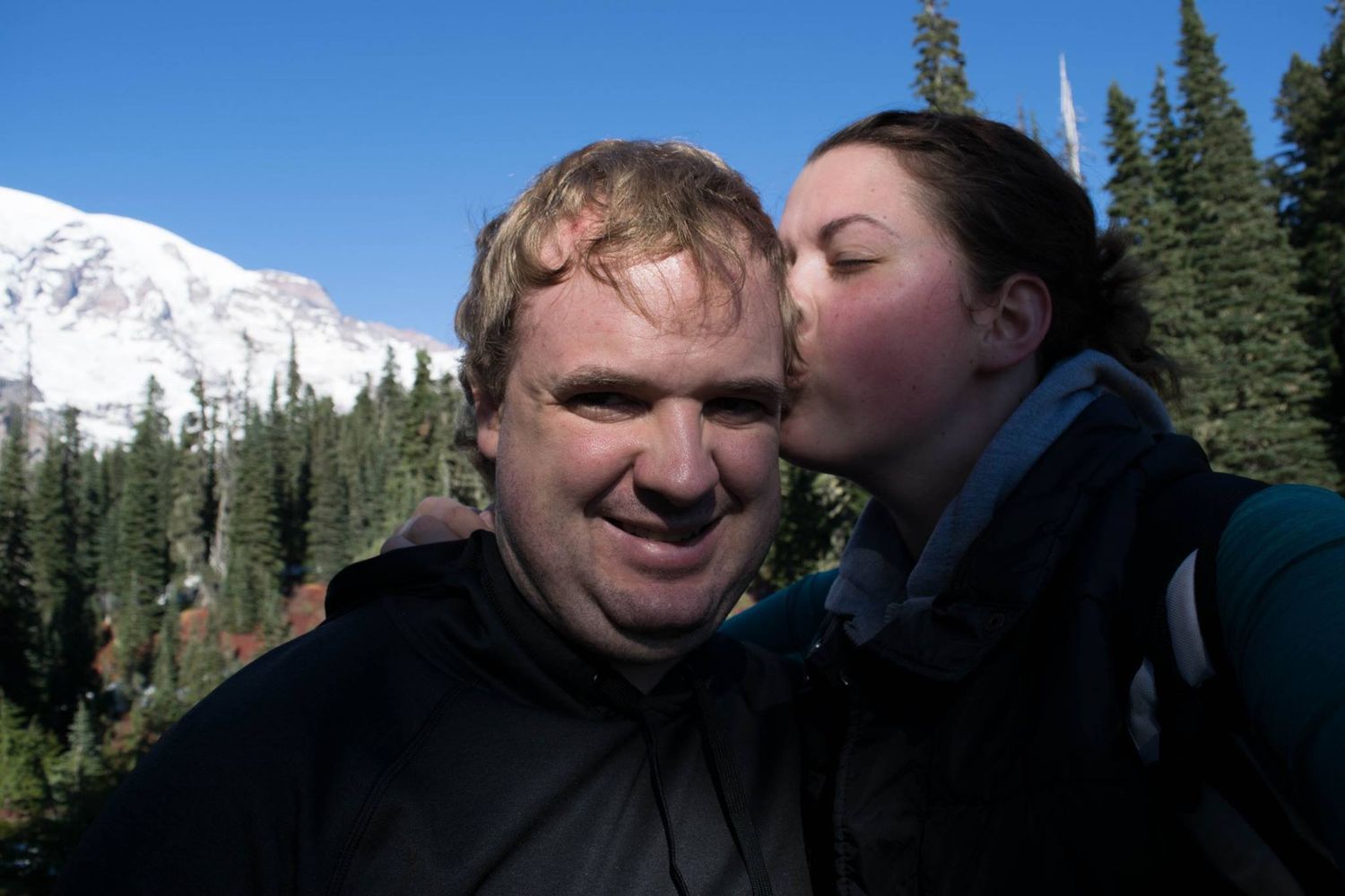 Two people share a moment with snow-capped mountain peaks in the background.