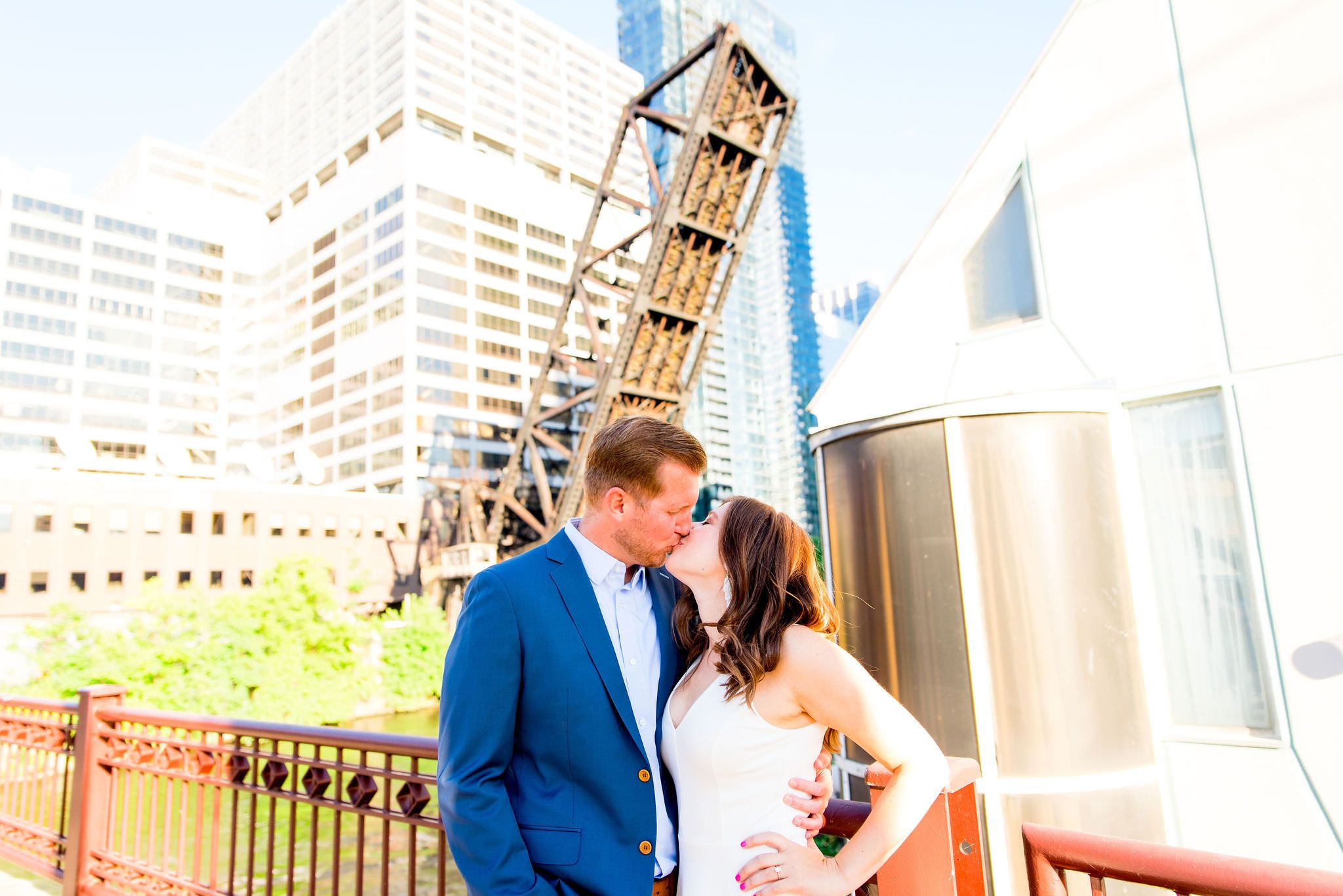 woman in white dress kissing man in navy suit in front of Chicago River at Kinzie St Bridge engagement pictures
