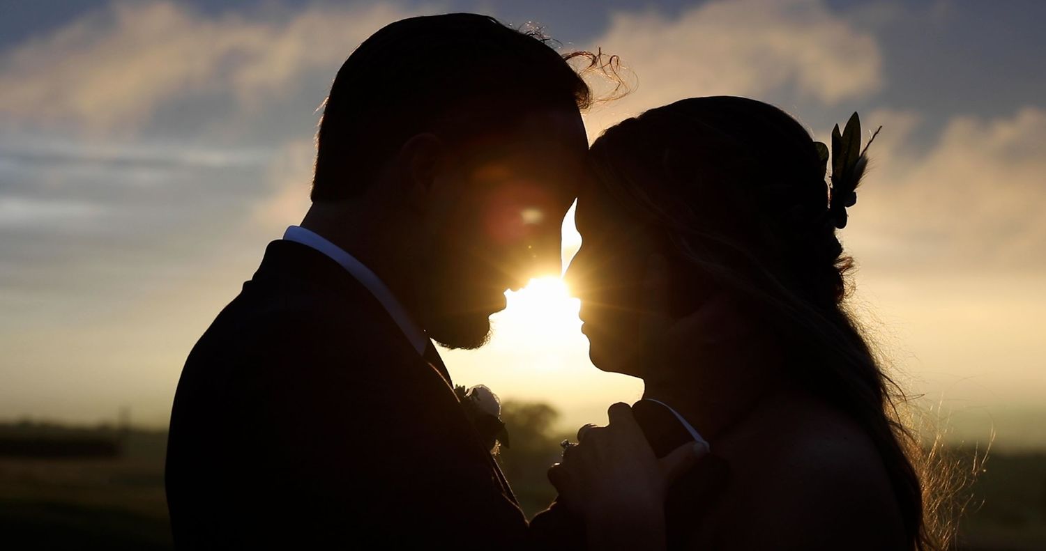 A silhouetted couple shares an intimate moment against a dramatic sunset sky.