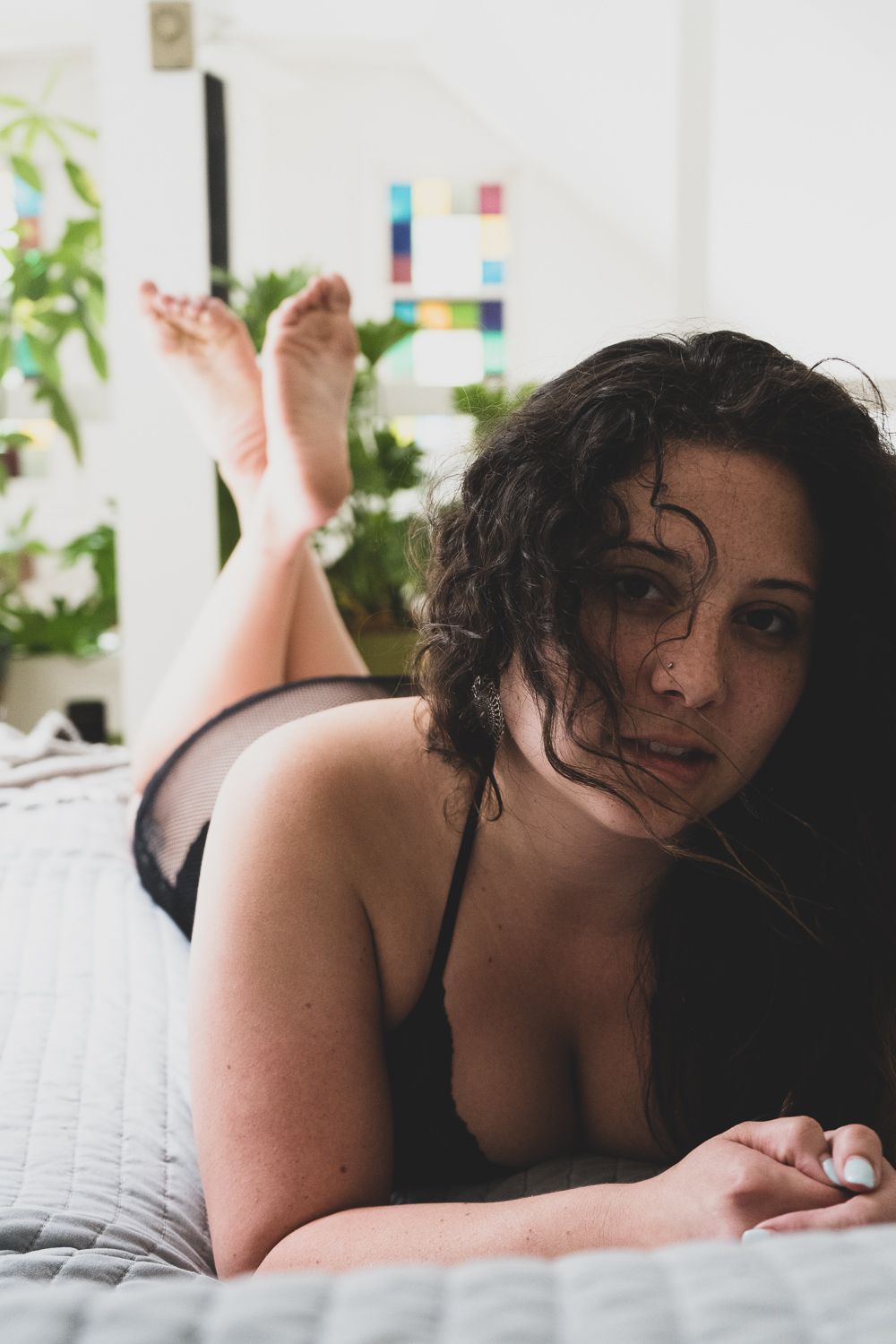 Brunette female laying on stomach during boudoir session in black mesh lingerie during in-home boudoir, boho session.