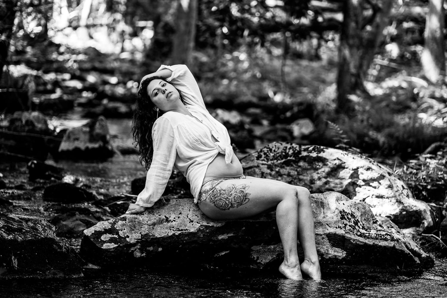 Outdoor boudoir session with girl on rock in creek arching with white tie shirt in Poconos Mountain