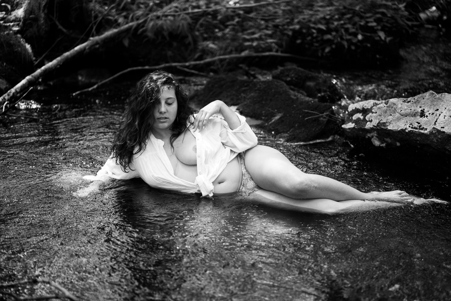 Brunette in white tie shirt laying in the river with only underwear and shirt, outdoor natural boho boudoir