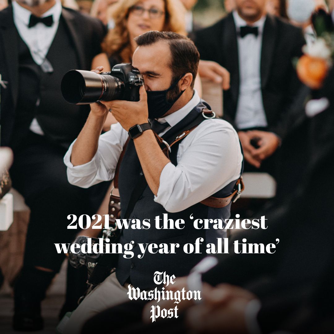 Wedding photographer wearing a face mask captures moments at a formal event with guests in black tie attire.