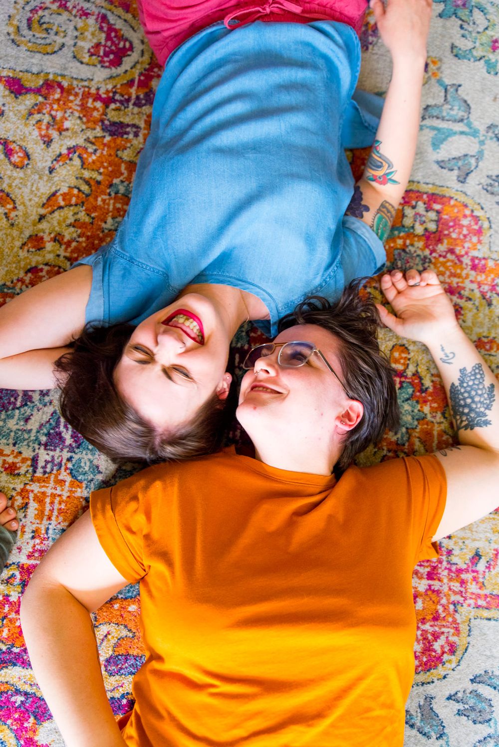 two woman laying on pink orange and blue rug with heads together, laughing for chicago couples pictures