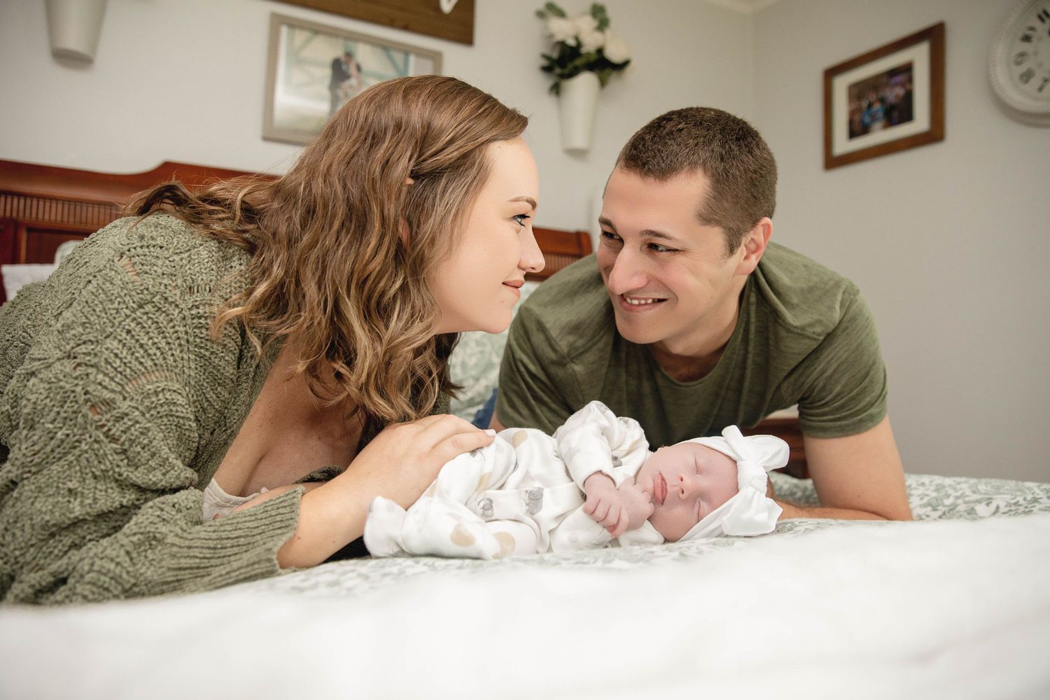 A tender family moment with a newborn baby lying on a white bed.