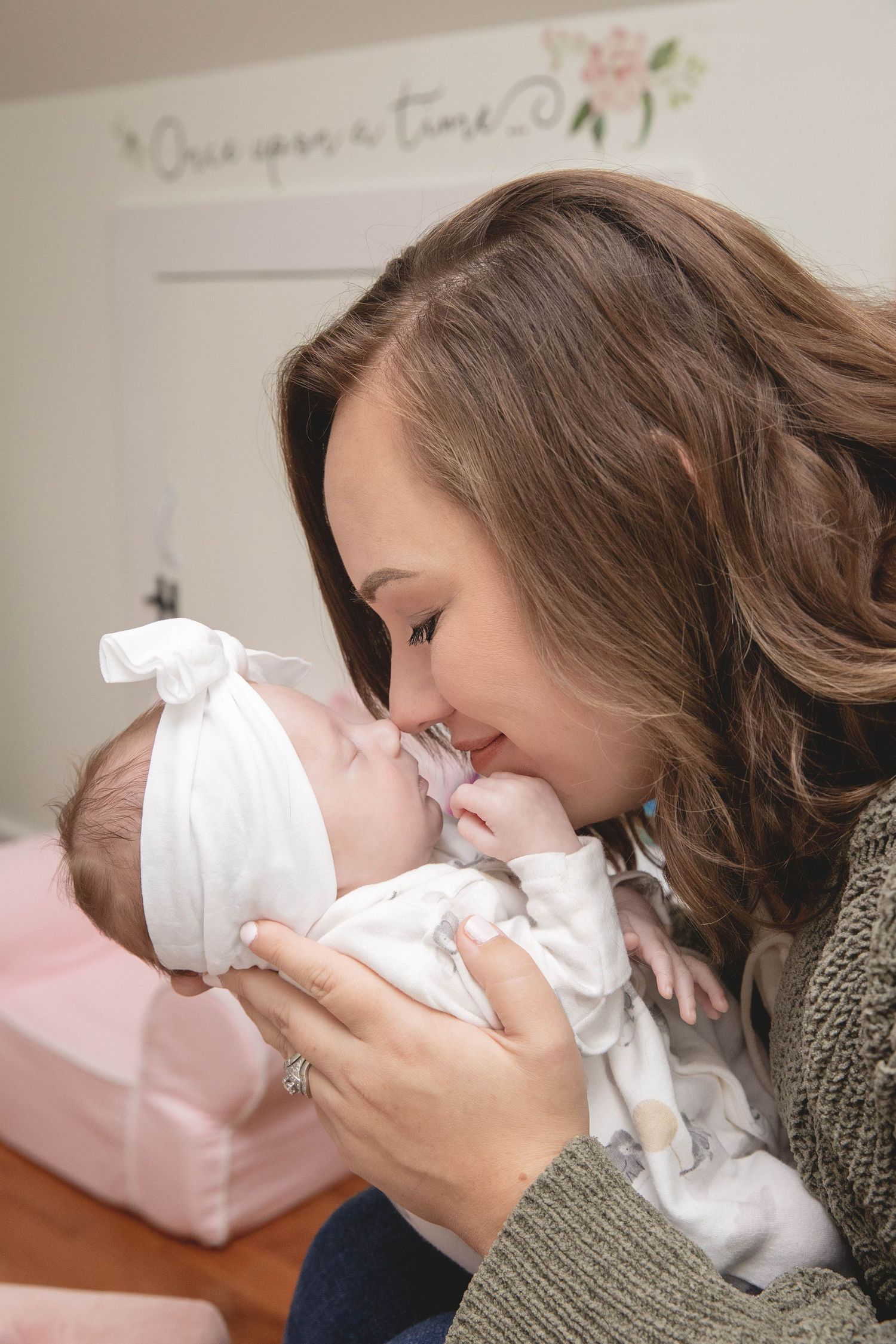 A mother in a knit sweater sharing an intimate moment with her baby against a pink backdrop.