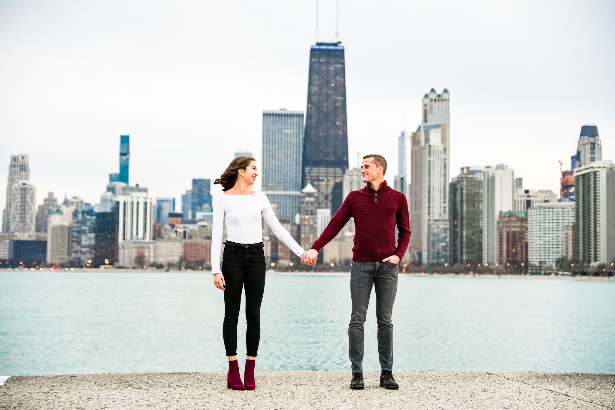 young couple in red and white holding hands on pier at North Avenue Beach engagement pictures in Chicago