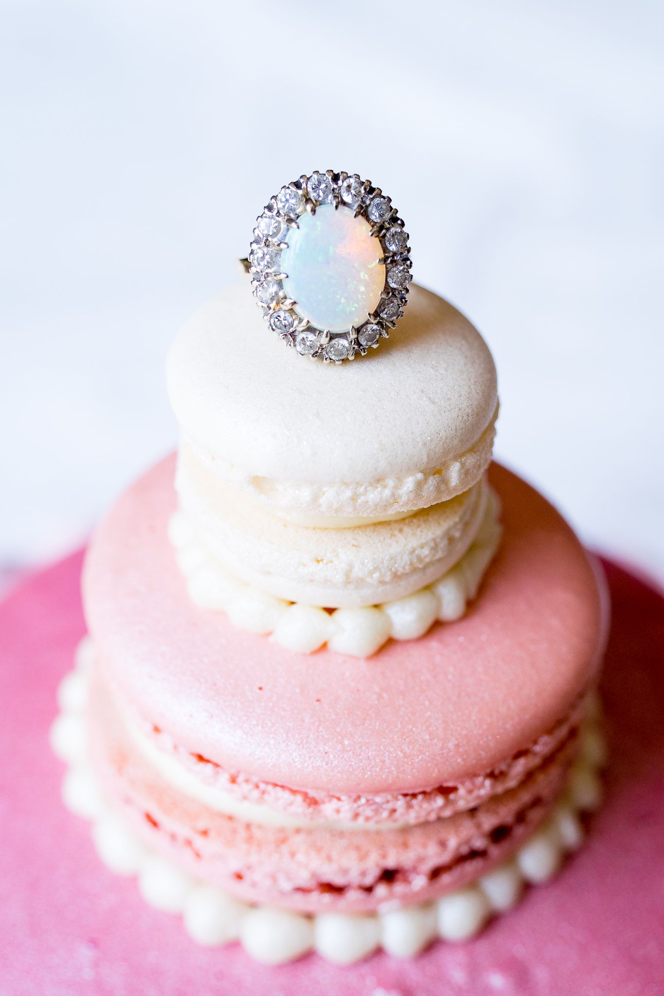 oval opal engagement ring on top of a tier giant macaron cake in pink and white