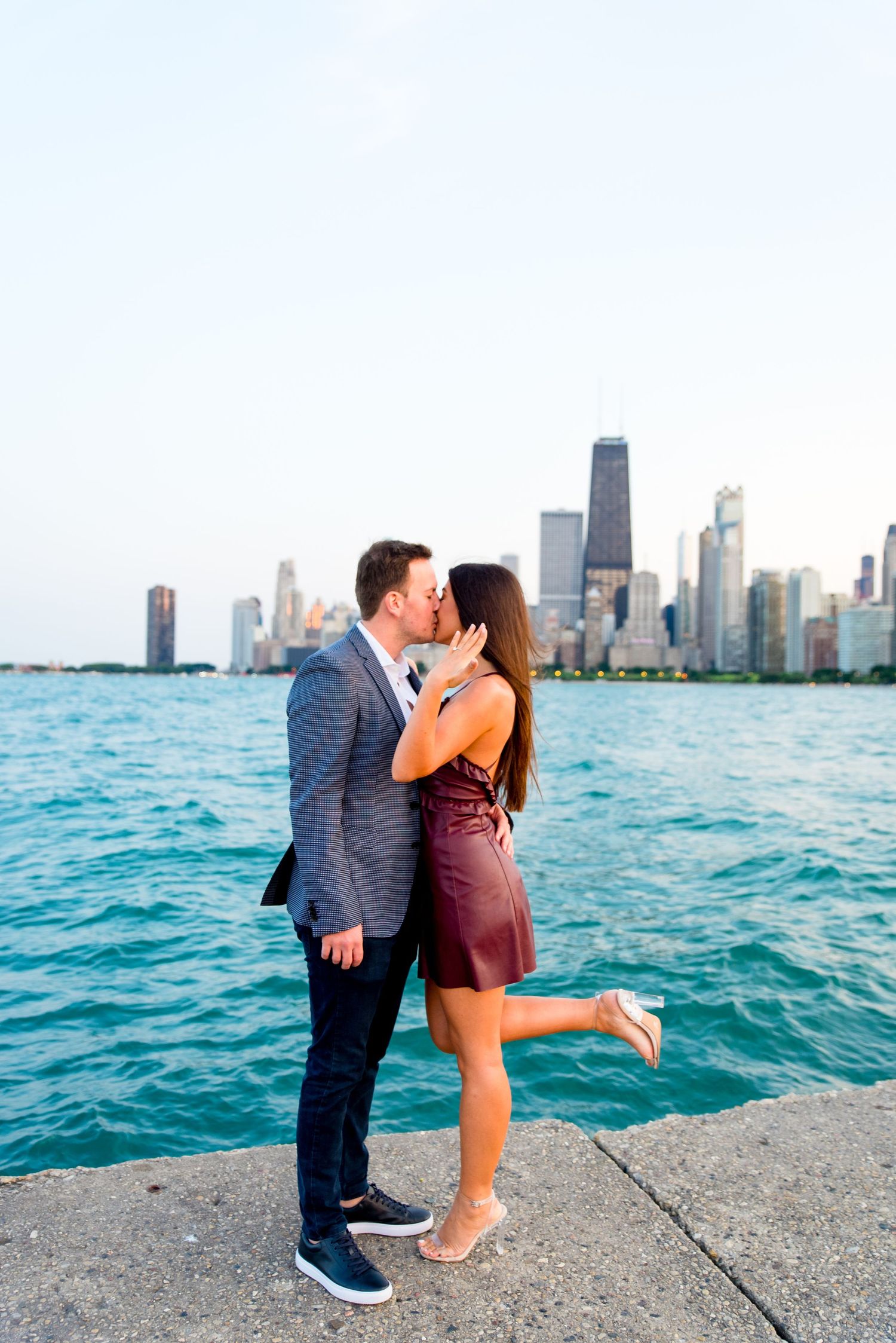 man and woman kissing and woman holding up hand in front of skyline after Chicago Proposal