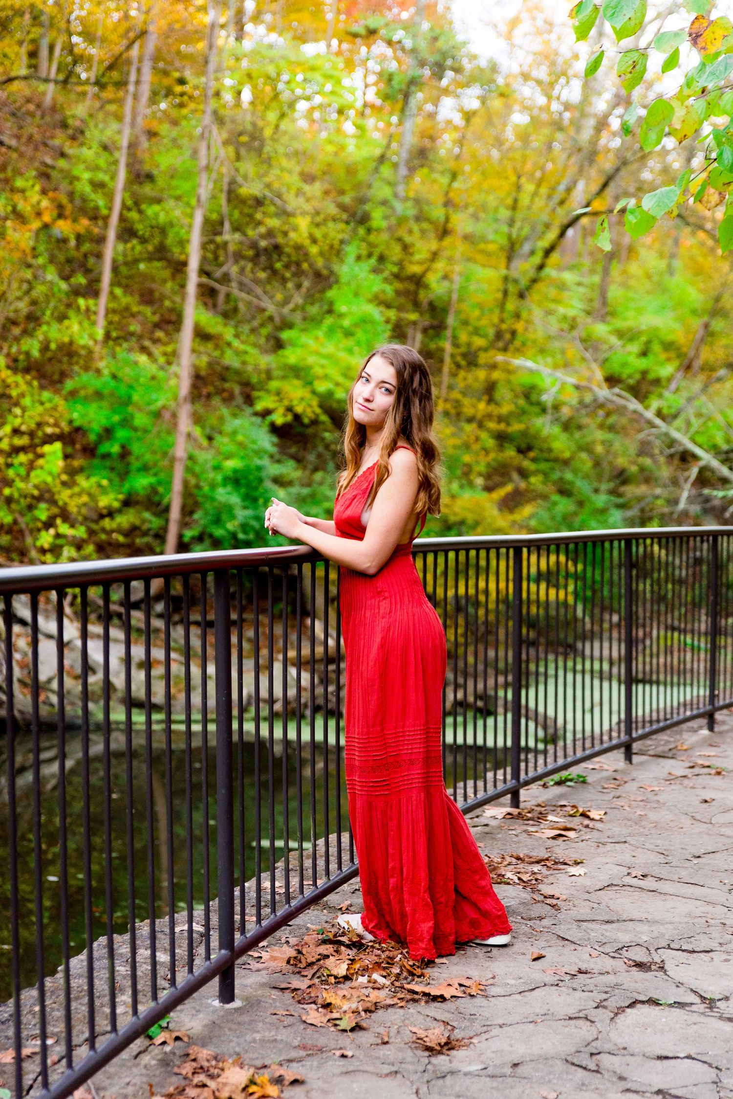 Senior Pictures in Chicago with a girl leaning over a bridge under fall colored trees next to a creek