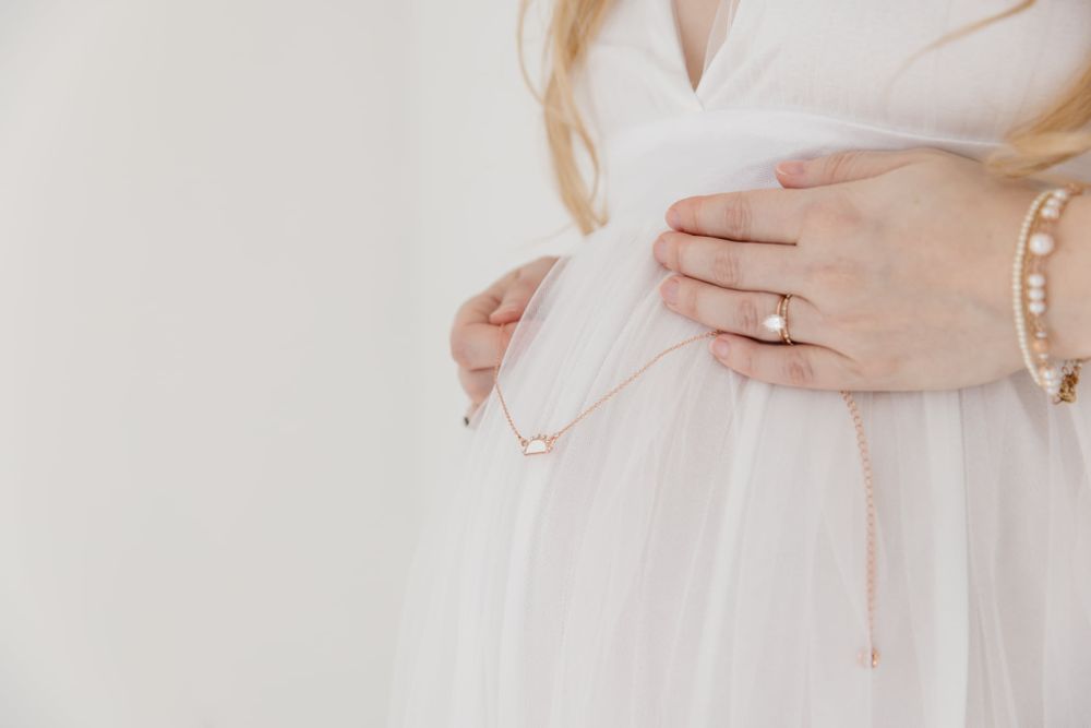 Close-up of hands with wedding ring resting on white tulle dress.