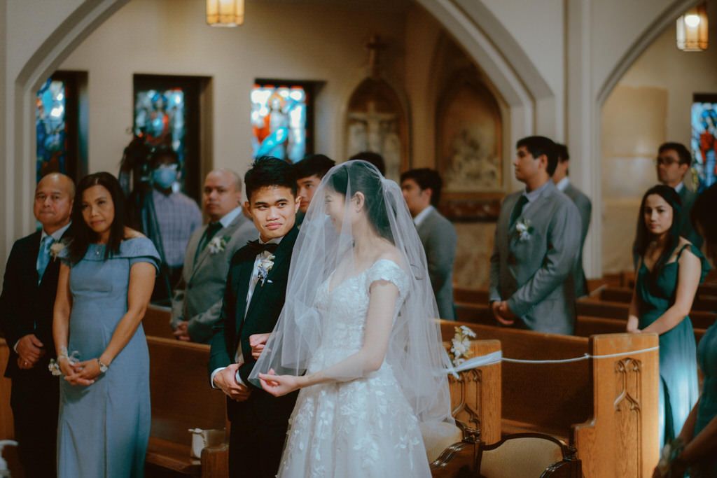 A wedding ceremony takes place in a traditional church with stained glass windows and wooden pews.