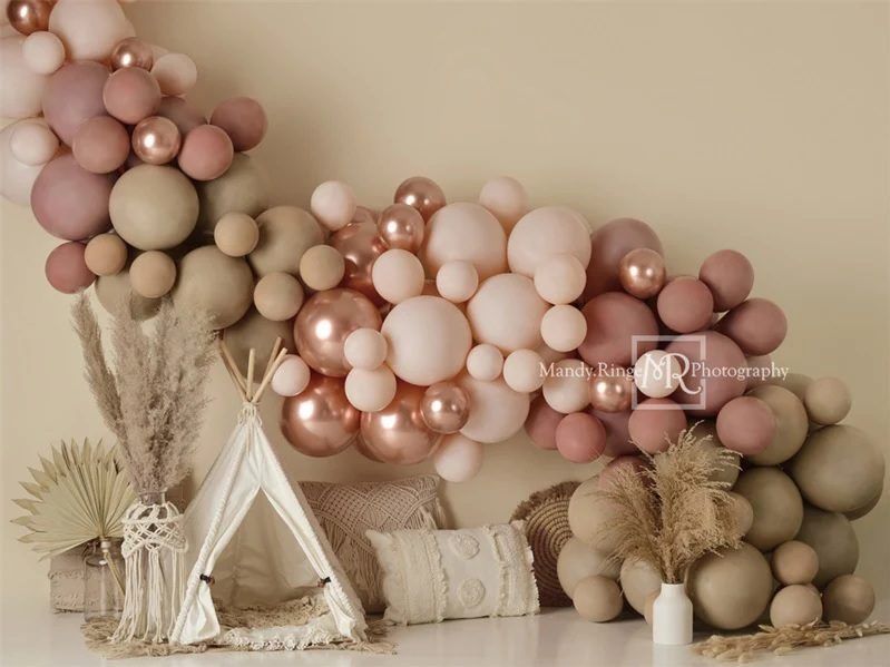 Elegant party backdrop with blush pink and neutral balloon garland above a teepee tent setup.