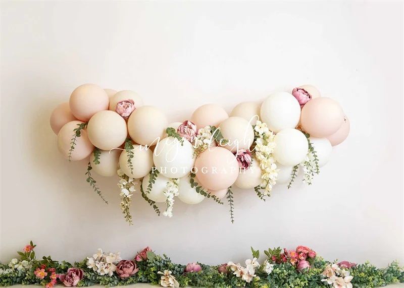 Elegant balloon garland in soft pastel colors with floral arrangements below against a white wall.