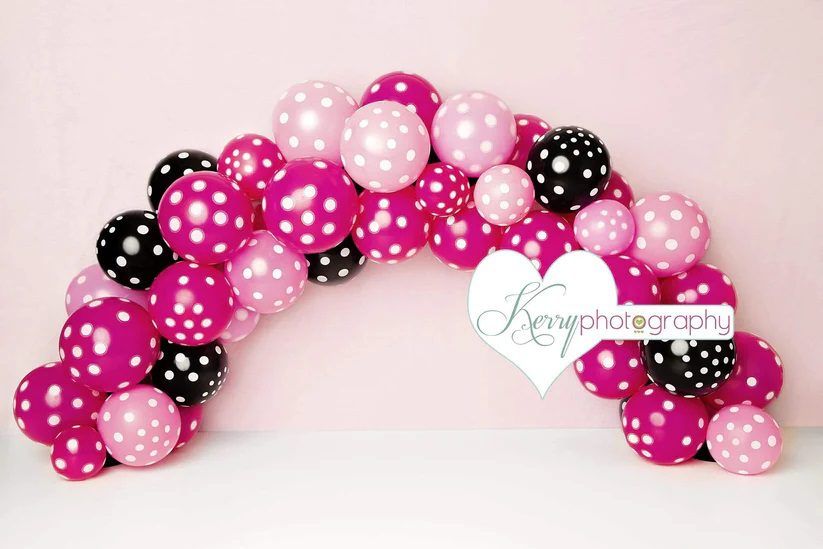Pink and black polka dot balloon arch decoration on light background.