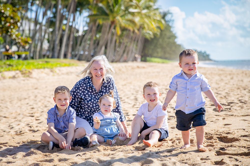 A loving grandma sits with her grandchildren on the beach at Palm Cove