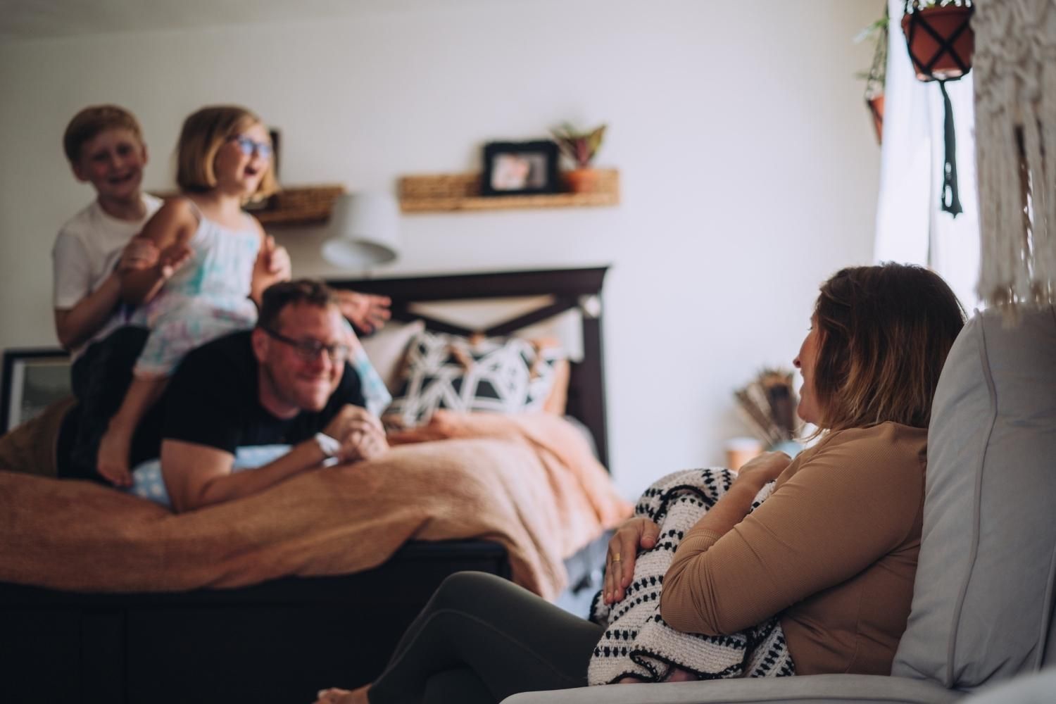 mom holds newborn and laughs at dad being silly with other two kids
